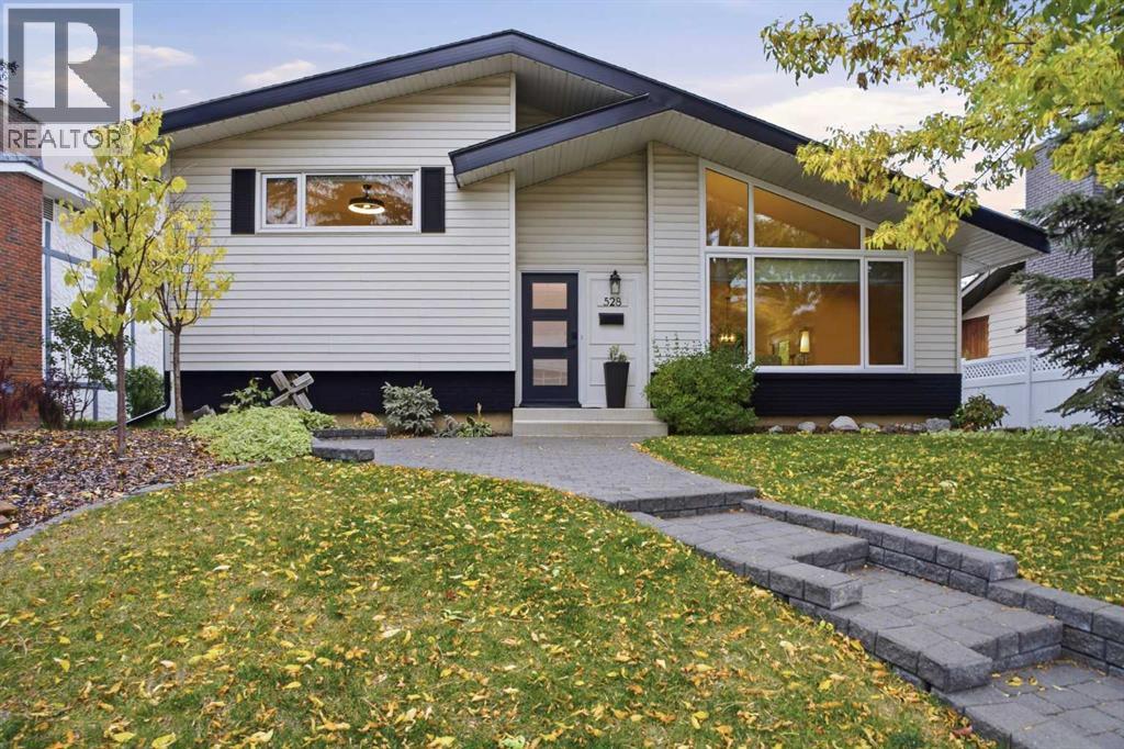 White bungalow with dark trim, a large front window, and a stone walkway across a leaf-strewn lawn.