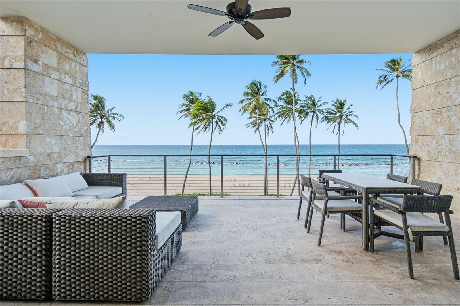 Furnished stone terrace overlooking a palm-lined beach and ocean.