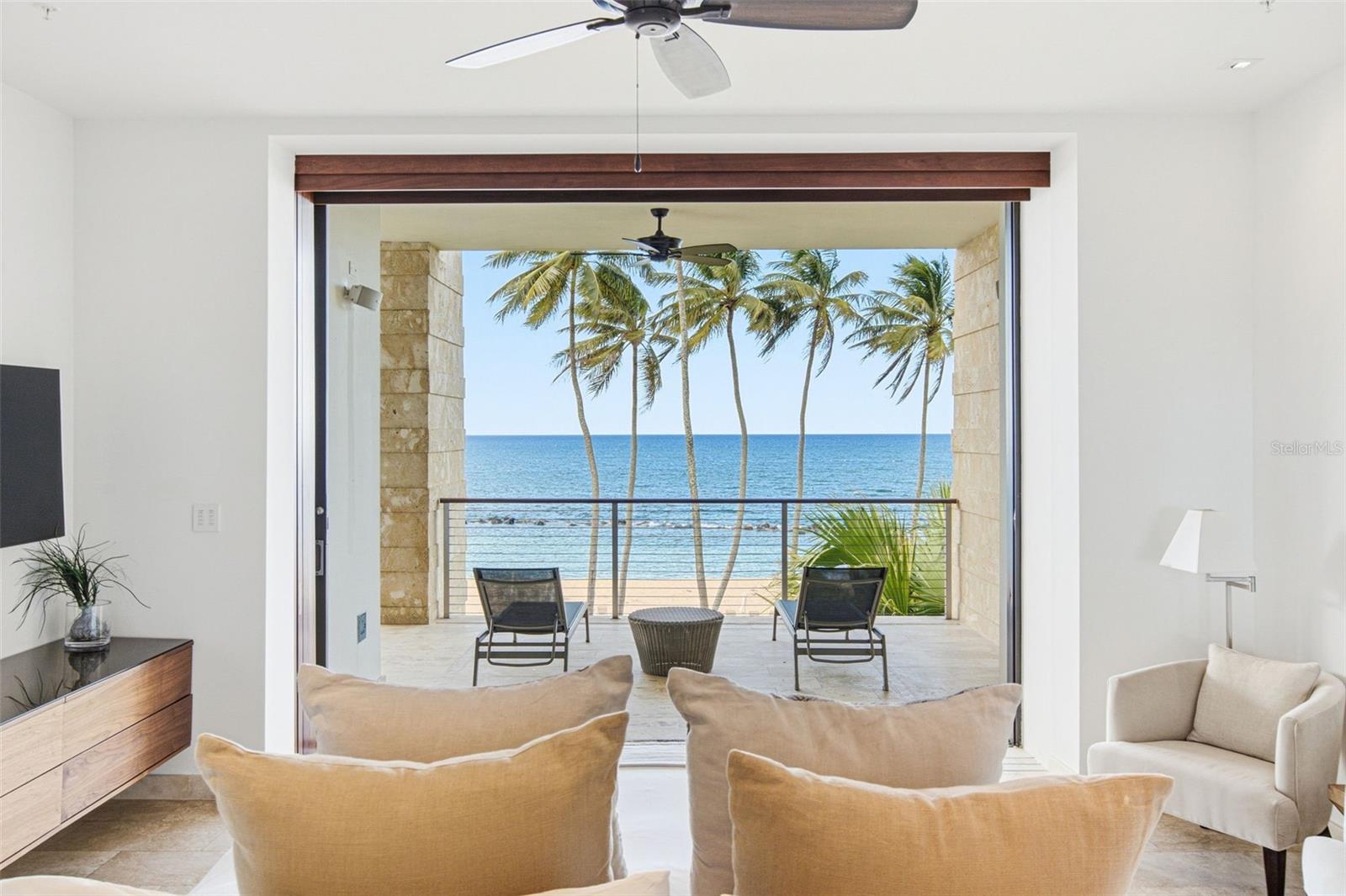 Furnished living room opens onto an oceanfront terrace with palm trees and a beach view.