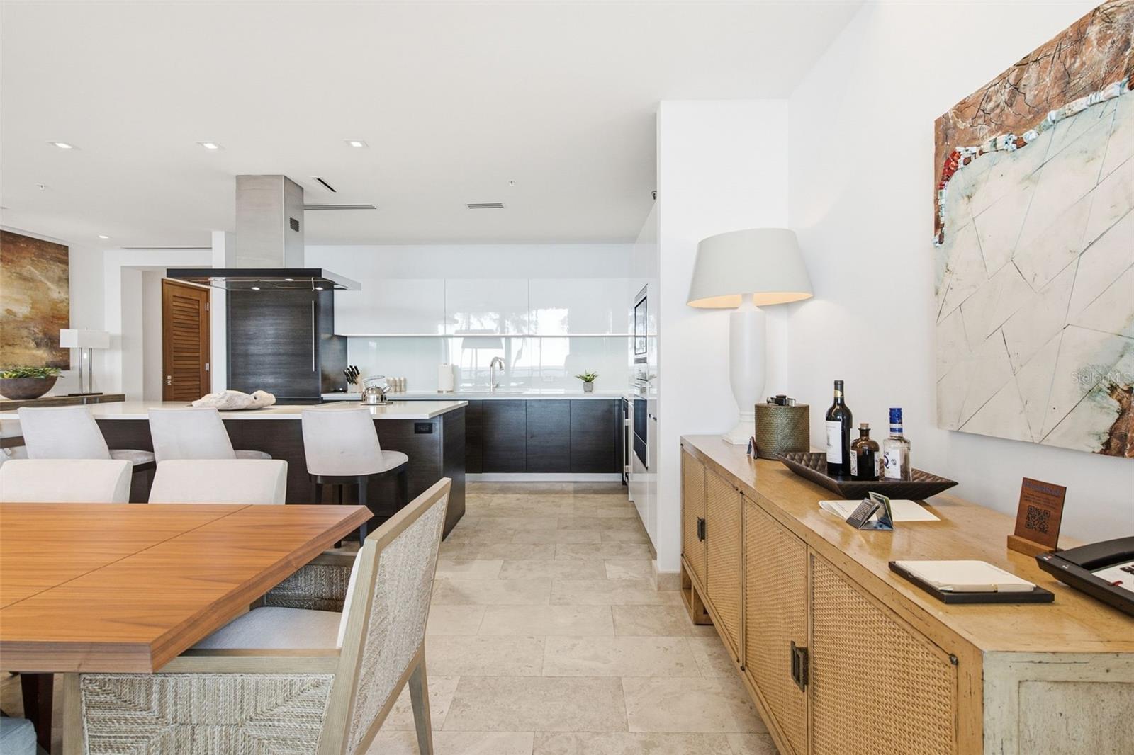 Open-plan kitchen and dining area with dark cabinetry, stone flooring, and a woven wood sideboard.
