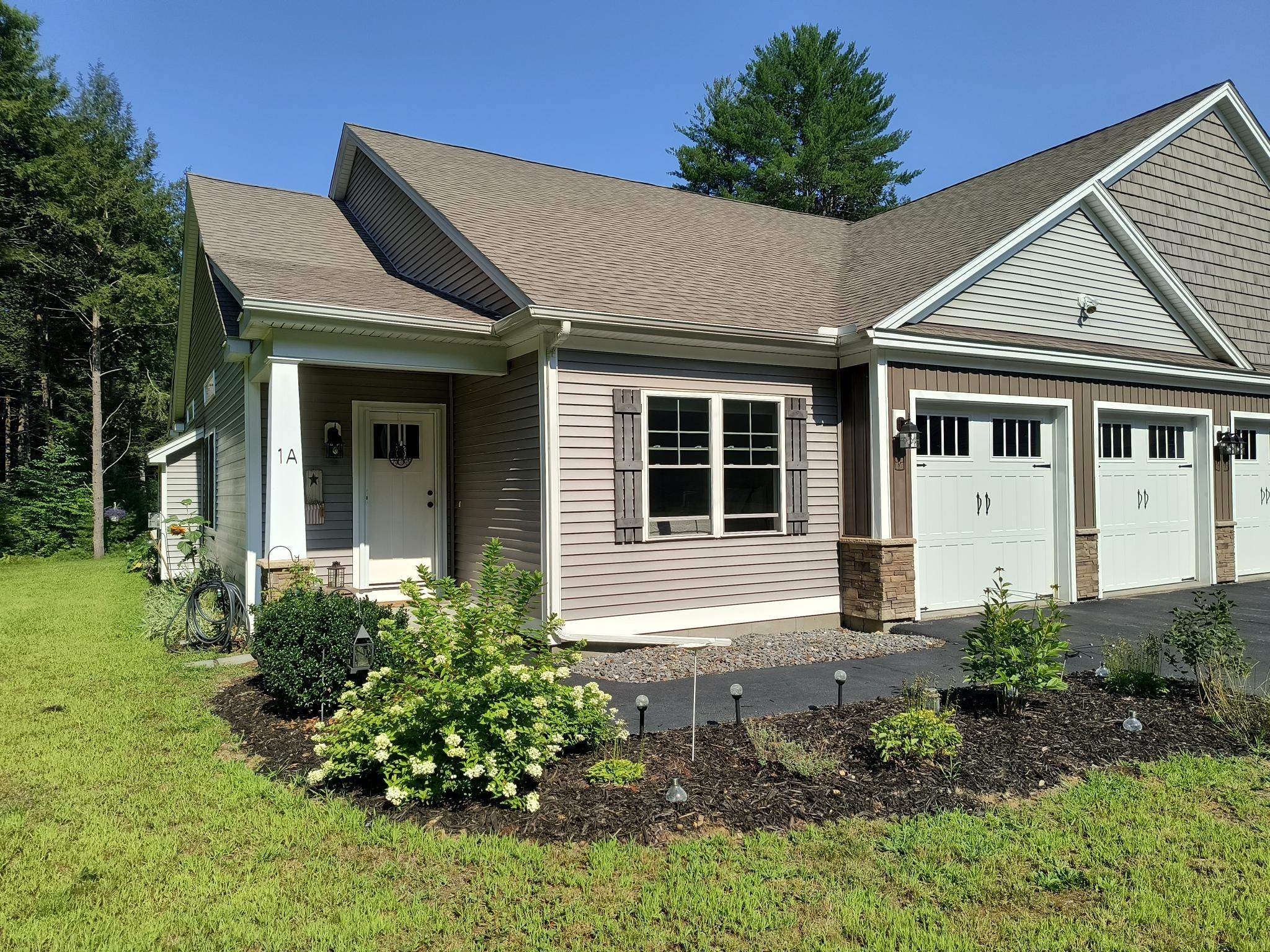 Gray-sided home marked 1A with a covered entry, two white garage doors, and landscaped front beds.