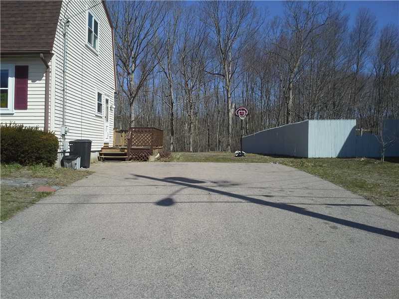 Paved driveway beside a white-sided house, with a basketball hoop and long gray storage structure.