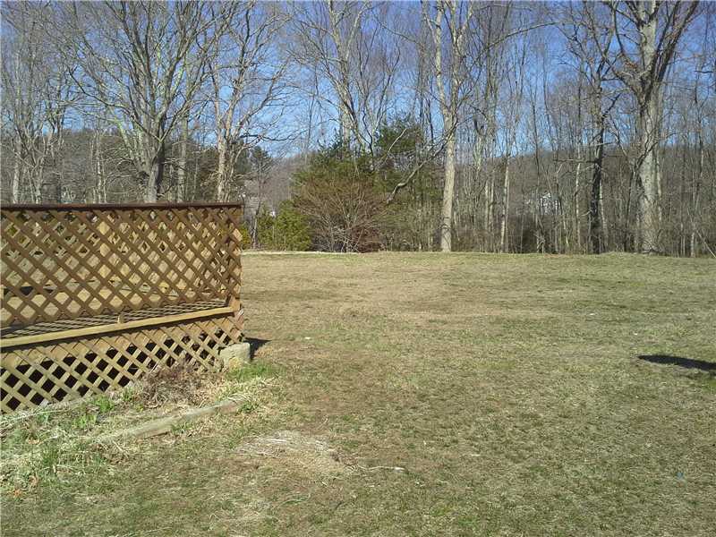 Backyard lawn bordered by leafless trees, with a lattice-sided wooden deck at left.