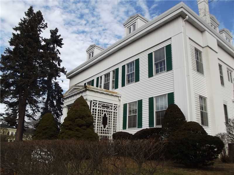 White clapboard house with green shutters and a decorative lattice entry, framed by mature trees and shrubs.
