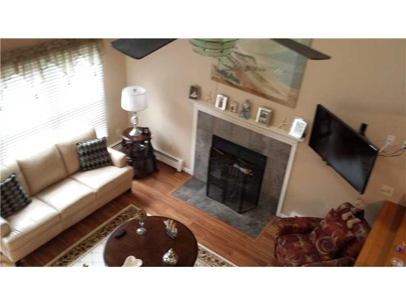 Living room with a stone fireplace, cream sofa, wall-mounted TV, and hardwood floors.