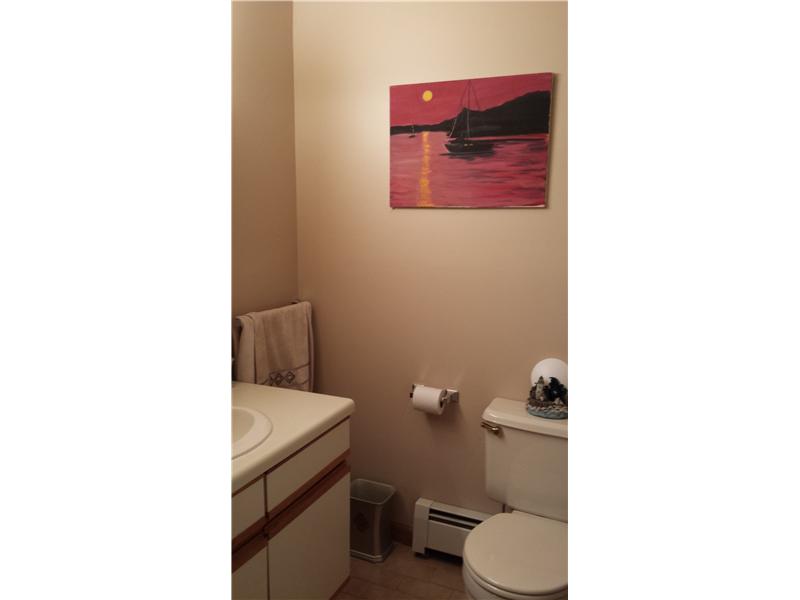 Bathroom with a white toilet, wood-trimmed vanity, and sailboat painting on the wall.