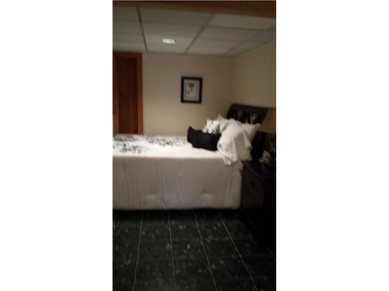 Bedroom with a white bed, dark tiled floor, and wood-paneled doorway.