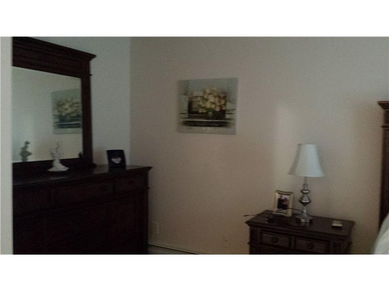 Bedroom with a dark wood dresser and mirror, bedside table, lamp, and edge of a bed.