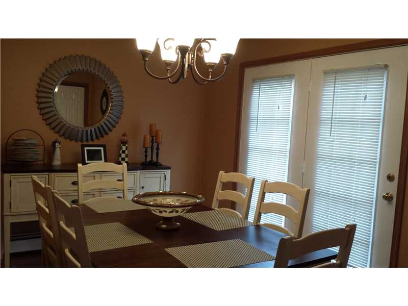 Dining room with a dark wood table, light chairs, sunburst mirror, and glass doors with blinds.