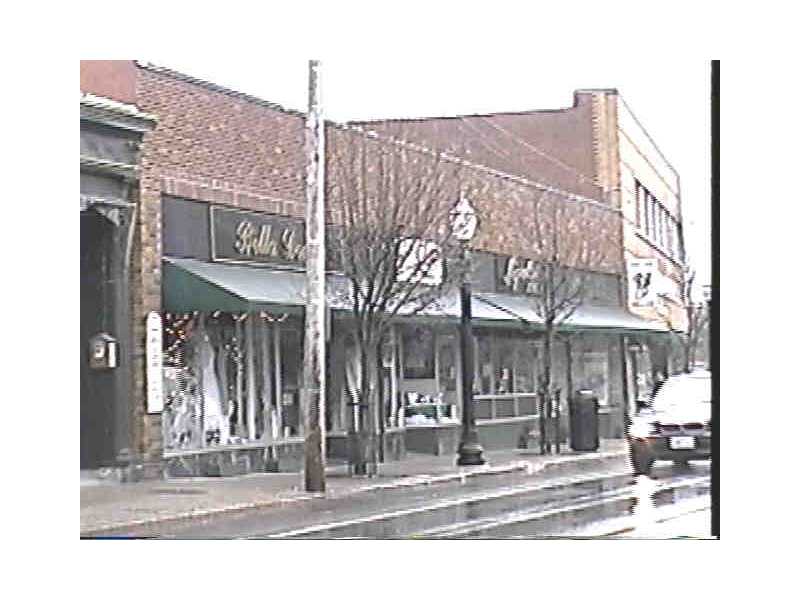 Brick commercial storefront with awnings and large display windows on a wet street.