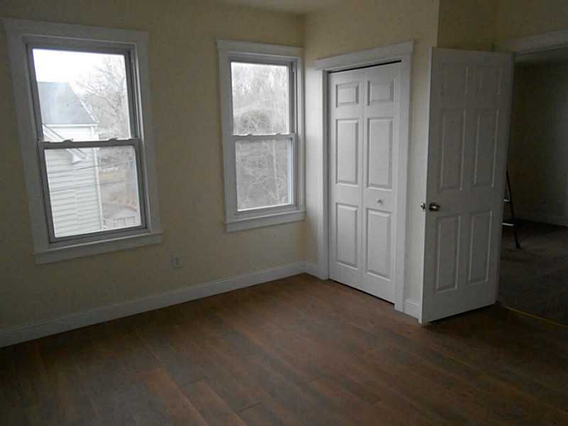 Empty room with two windows, dark wood flooring, and an open paneled door.