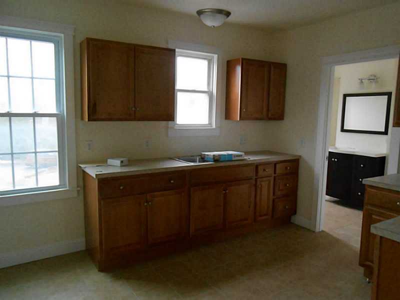 Kitchen with brown wood cabinets, light countertops, and a sink beneath a window.