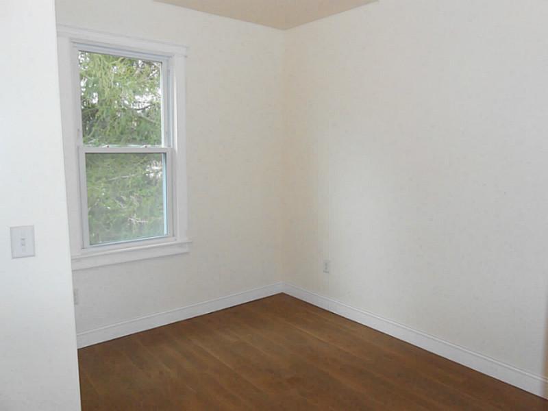 Empty room with wood flooring and a window overlooking trees.