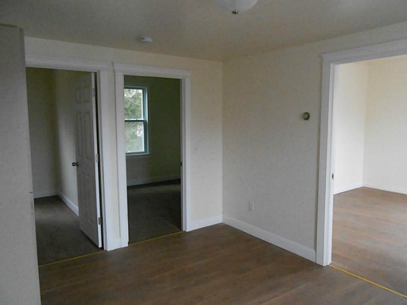 Vacant room with hardwood floors and open doorways to adjoining rooms.