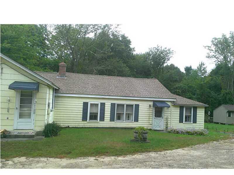 Pale yellow single-story house with dark shutters and a gravel driveway