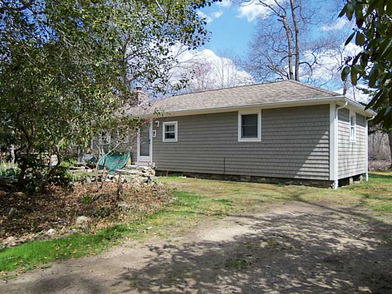 Single-story gray-sided house with a side door, windows, and patchy lawn.