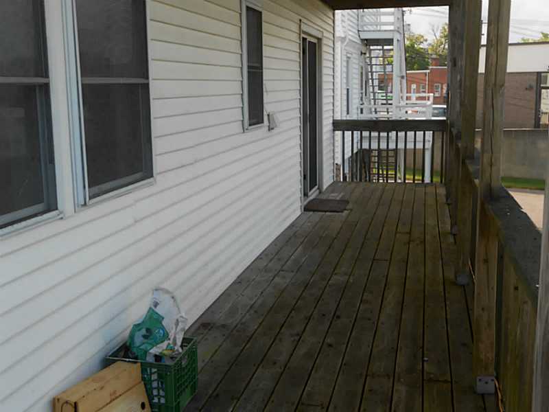 Covered wooden porch beside a white-sided building, with windows and a railing.