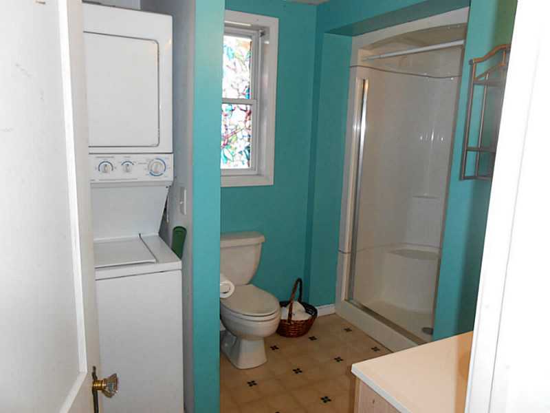 Bathroom with turquoise walls, glass shower, stacked washer and dryer, and stained-glass window.