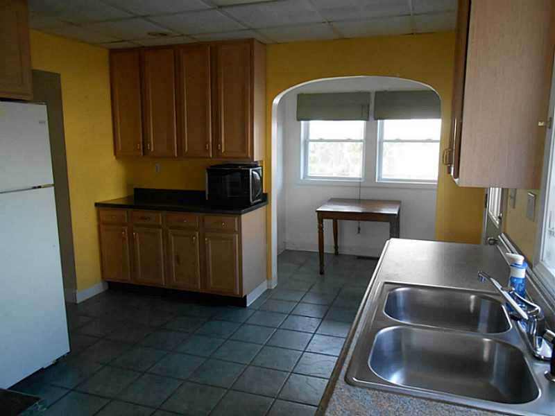 Kitchen with wood cabinets, tiled floor, double sink, and a small table by the windows.