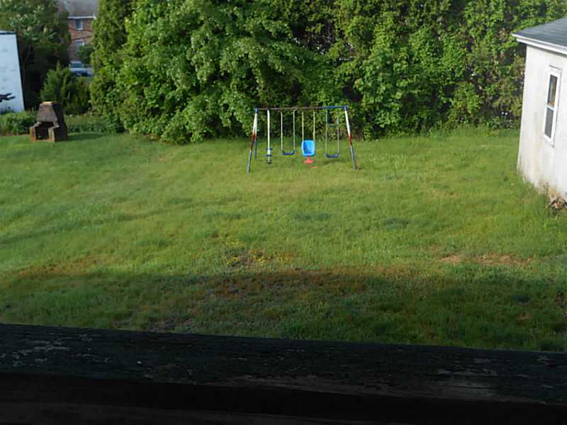 Backyard lawn with a metal swing set, blue toddler swing, and dense trees.