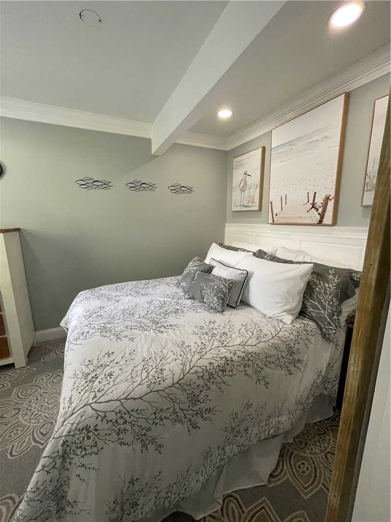 Bedroom with branch-patterned bedding, a white paneled headboard, and coastal artwork.