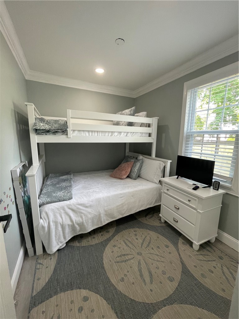 Bedroom with a white bunk bed, patterned rug, and dresser with a television beside the window.