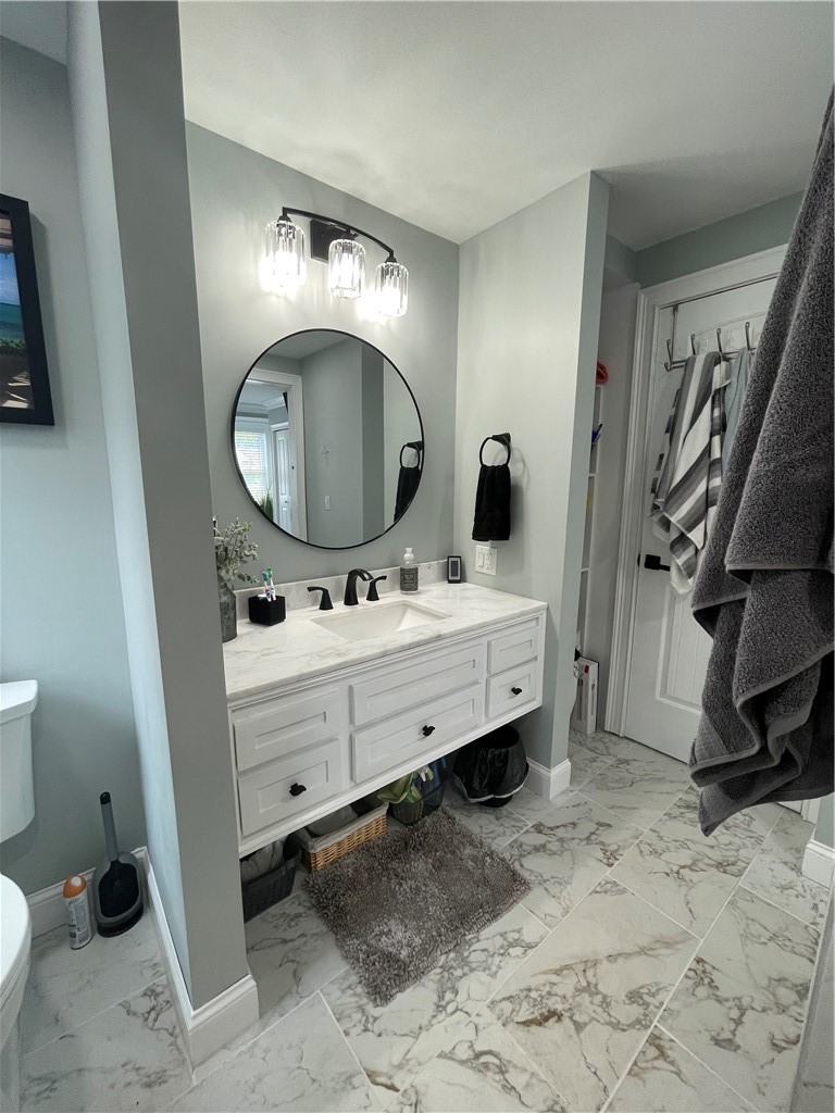 Bathroom with a white double-sink vanity, round mirror, and marble-look tile.