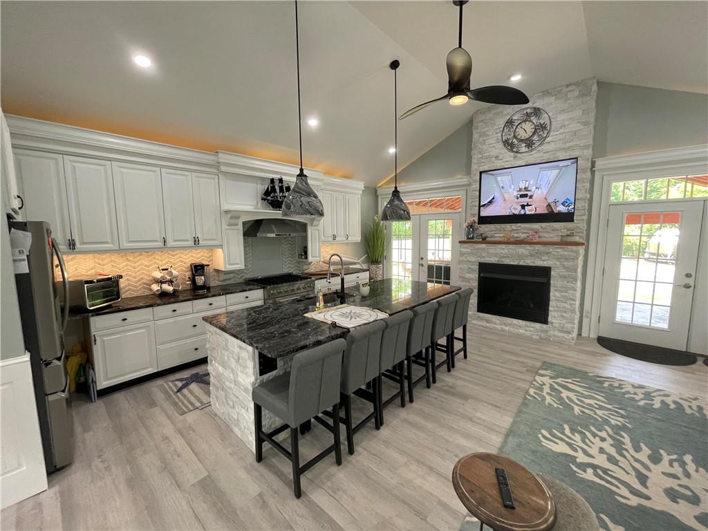 Kitchen with white cabinets, a dark stone island, bar seating, and a stone fireplace.