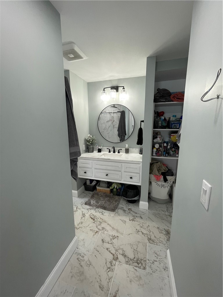 Bathroom with a white vanity, round mirror, marble-look tile, and open storage shelves.