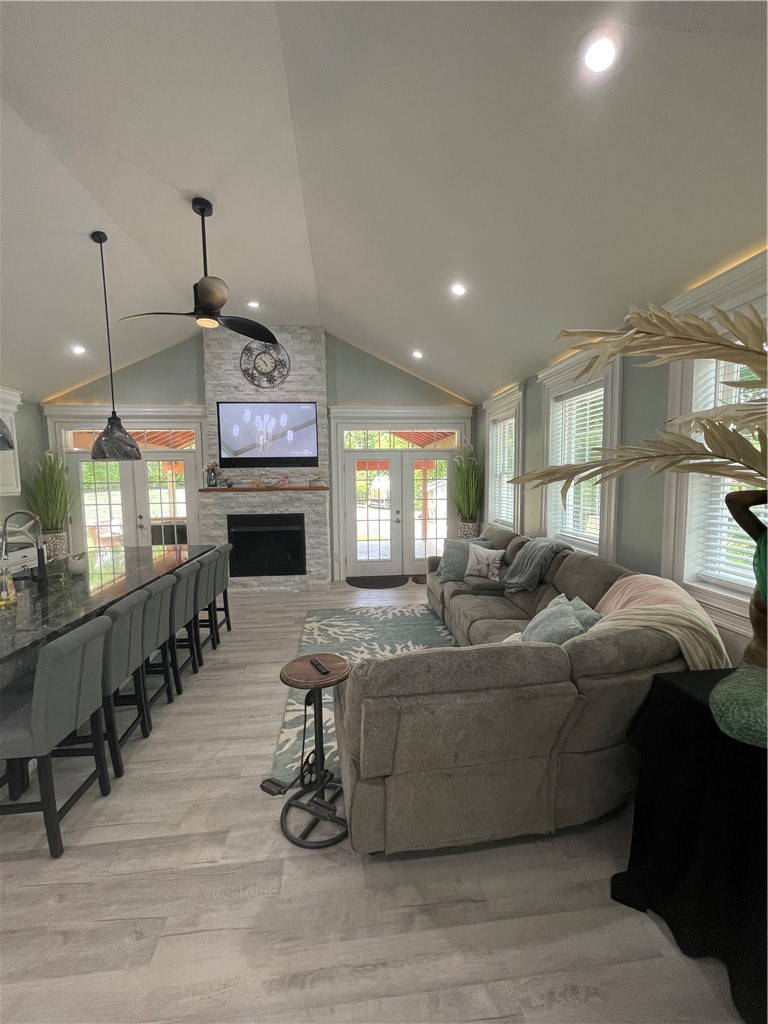 Open-plan living room with vaulted ceiling, gray sectional, stone fireplace, and glass doors to the patio.