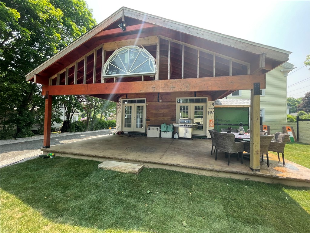 House with an unfinished timber-framed covered patio, arched upper window, outdoor dining set, and grill.