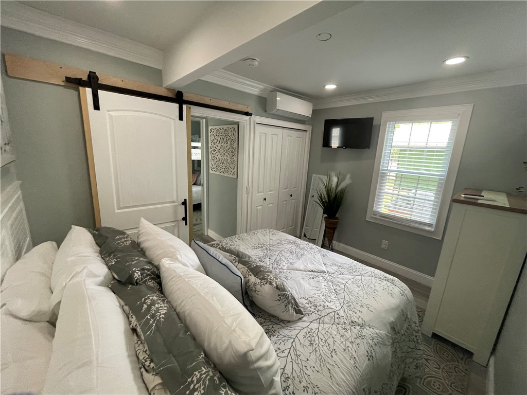 Furnished bedroom with patterned bedding, a white sliding barn door, and a window with blinds.