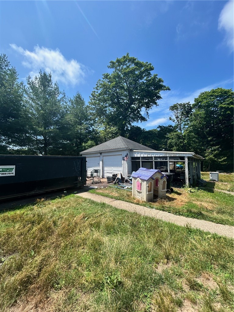 Detached garage and open-sided shed beside a grassy yard, with a dumpster and children's playhouse.