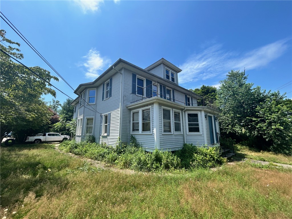 Gray multi-story house with white trim, an upper balcony, and a projecting enclosed porch.