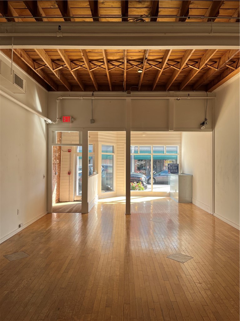 Vacant commercial storefront with hardwood flooring, exposed timber ceiling, and large street-facing windows.