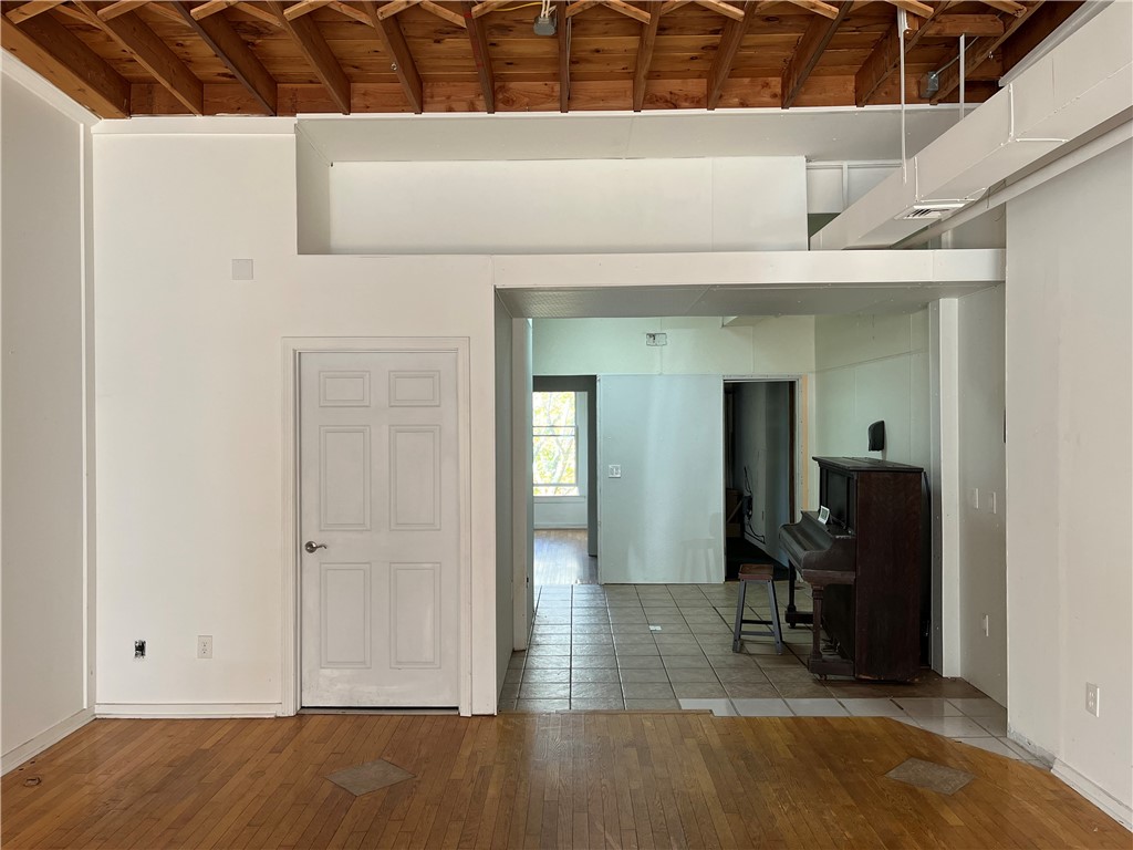 Open interior with exposed wooden ceiling joists, hardwood floors, and an upright piano.
