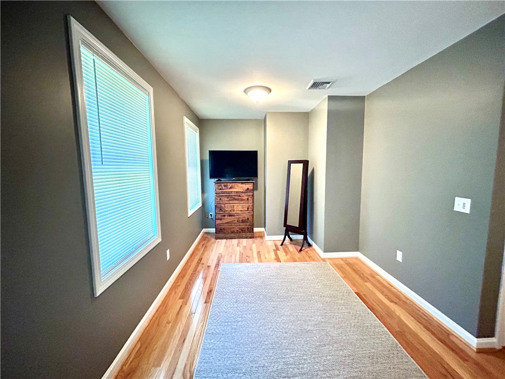 Narrow room with hardwood floors, a pale rug, and a television on a wooden dresser.