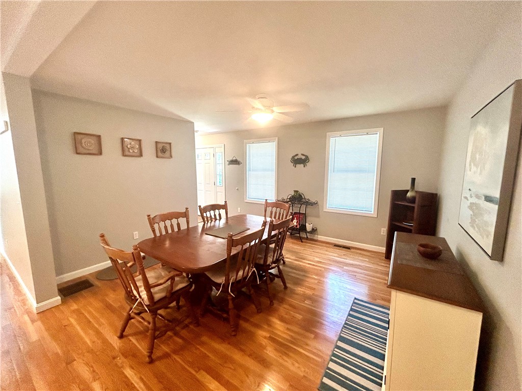 Dining room with a wooden table, chairs, hardwood floors, and two windows.