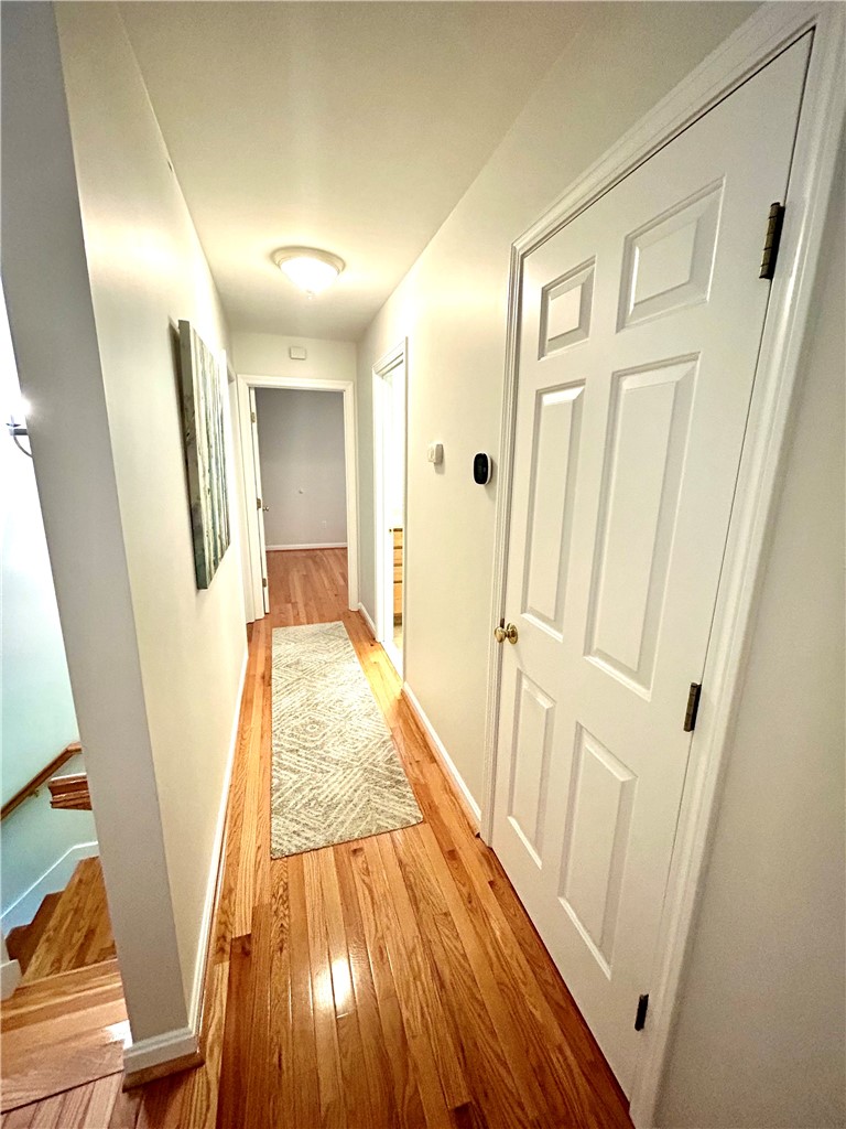 Hallway with polished hardwood floors, a patterned runner, and stairs at the left.