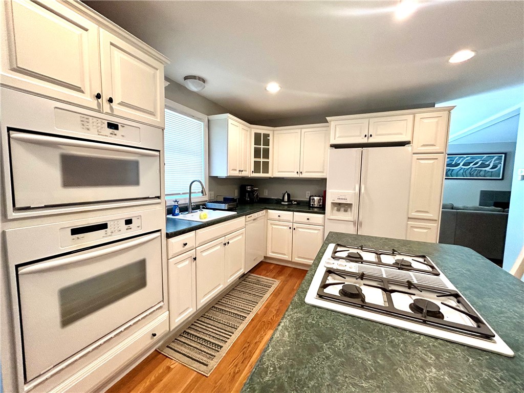 Kitchen with white cabinetry, dark green counters, a gas cooktop island, and double wall ovens.