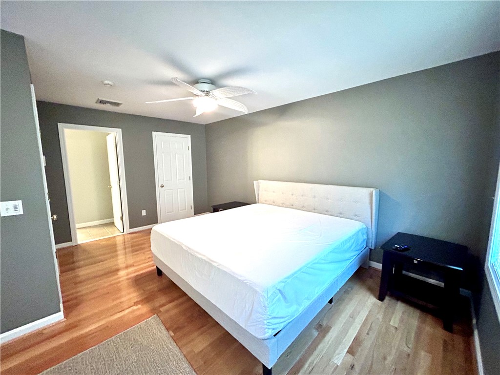Bedroom with a white bed, gray walls, ceiling fan, and mixed-tone wood floors.