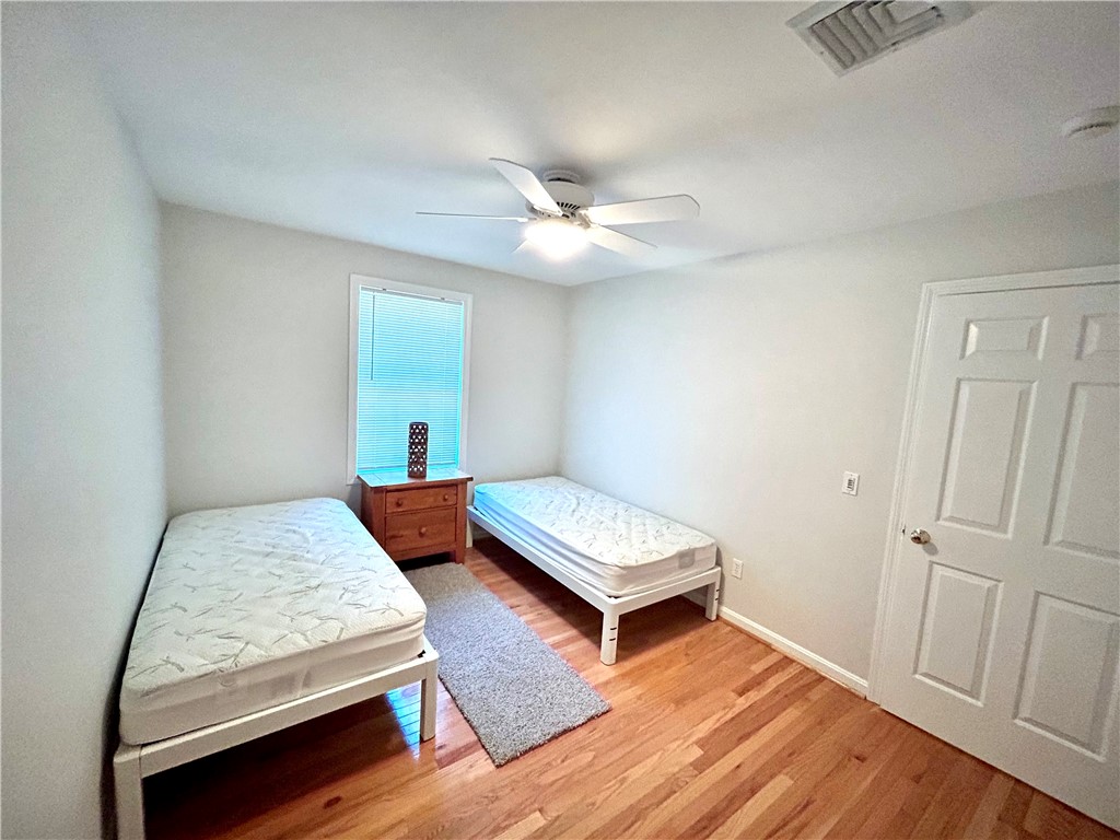 Bedroom with two single beds, hardwood floors, a ceiling fan, and a window with blinds.