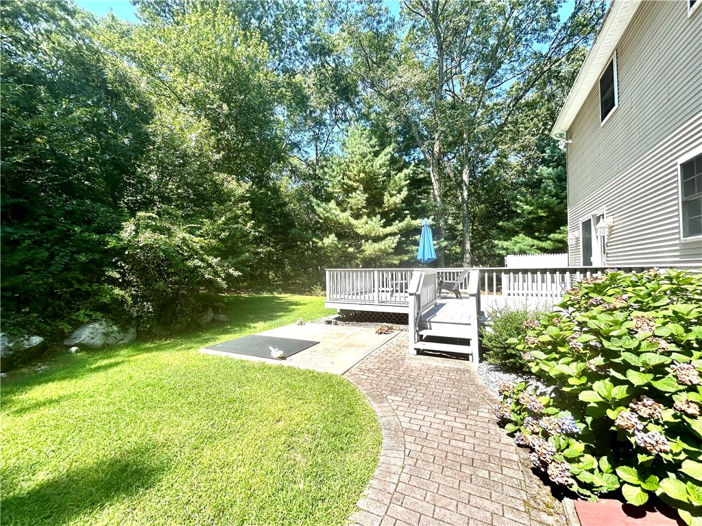 Backyard with a raised deck, blue umbrella, curved brick walkway, and mature trees.