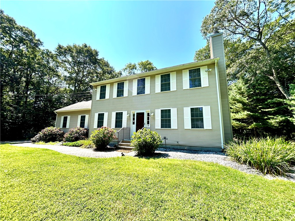 Two-story beige house with white shutters, a front entry, and a broad green lawn.