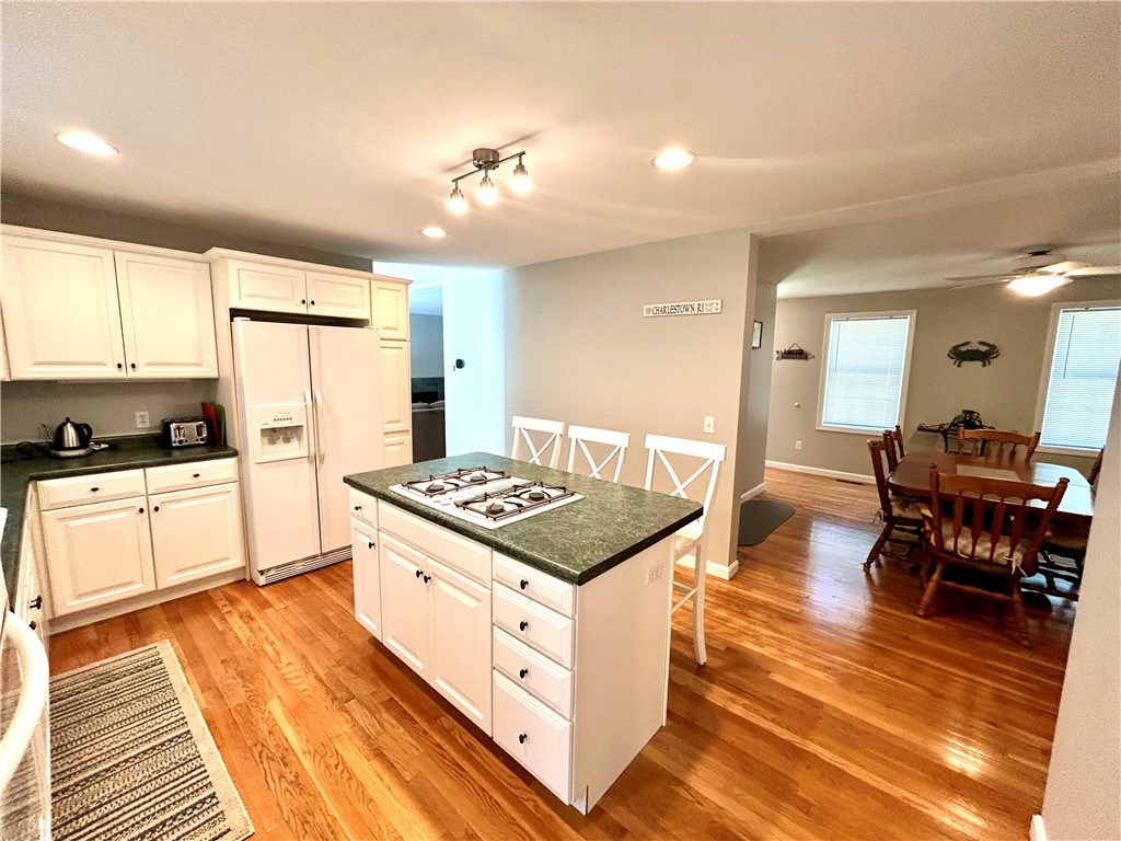 Kitchen with white cabinets, a cooktop island, hardwood floors, and an adjoining dining area.