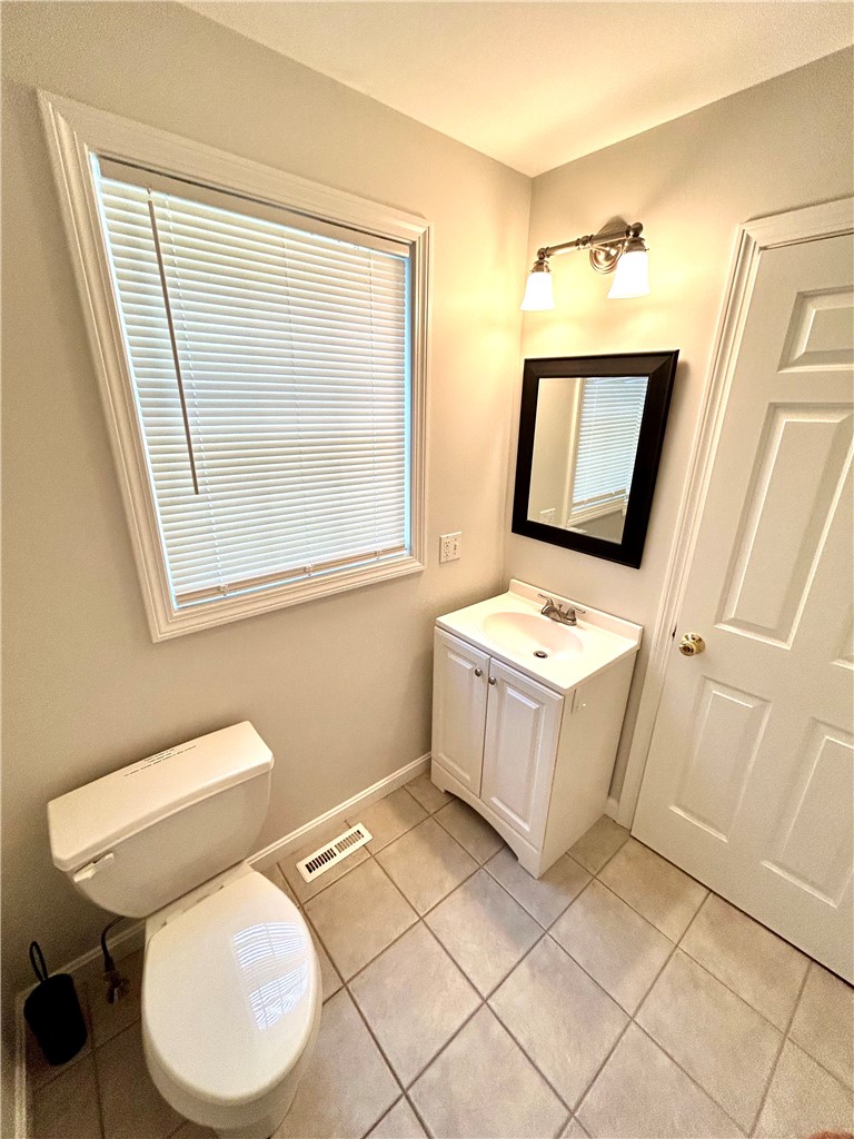 Bathroom with a white vanity and toilet, tiled floor, and a window with closed blinds.