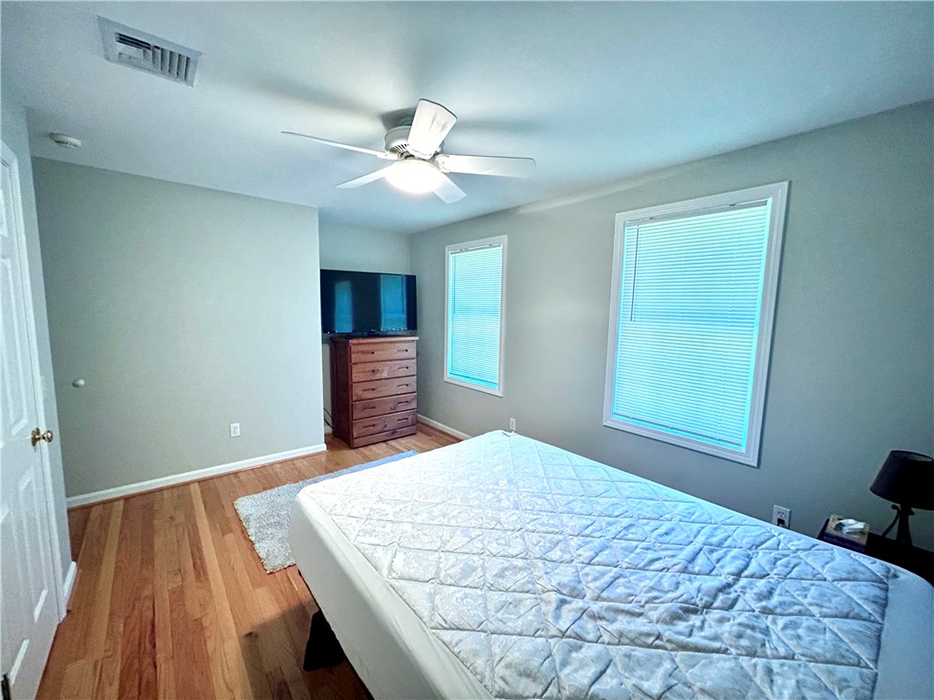 Bedroom with a bed, hardwood floors, and two windows with blinds.