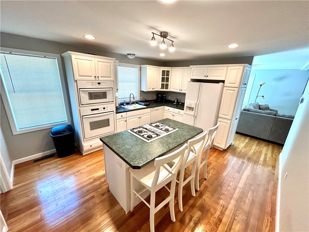 Kitchen with white cabinets, double ovens, and a green island with cooktop and seating.