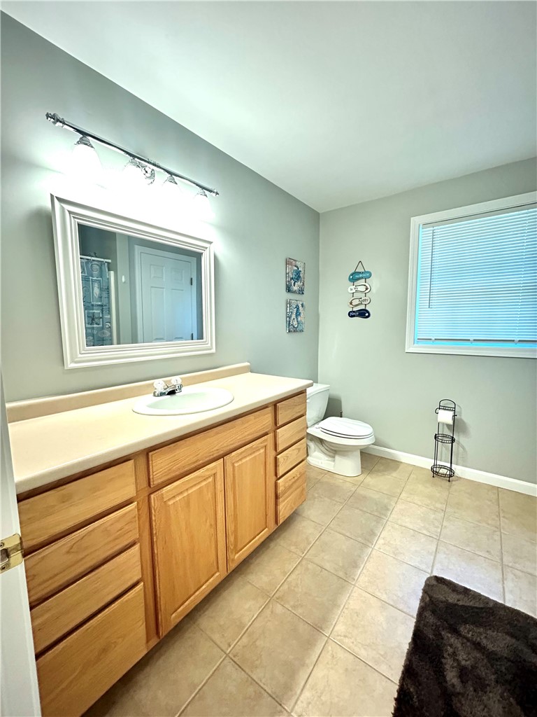 Bathroom with a long wood vanity, cream countertop, and tiled floor beside a window with blinds.