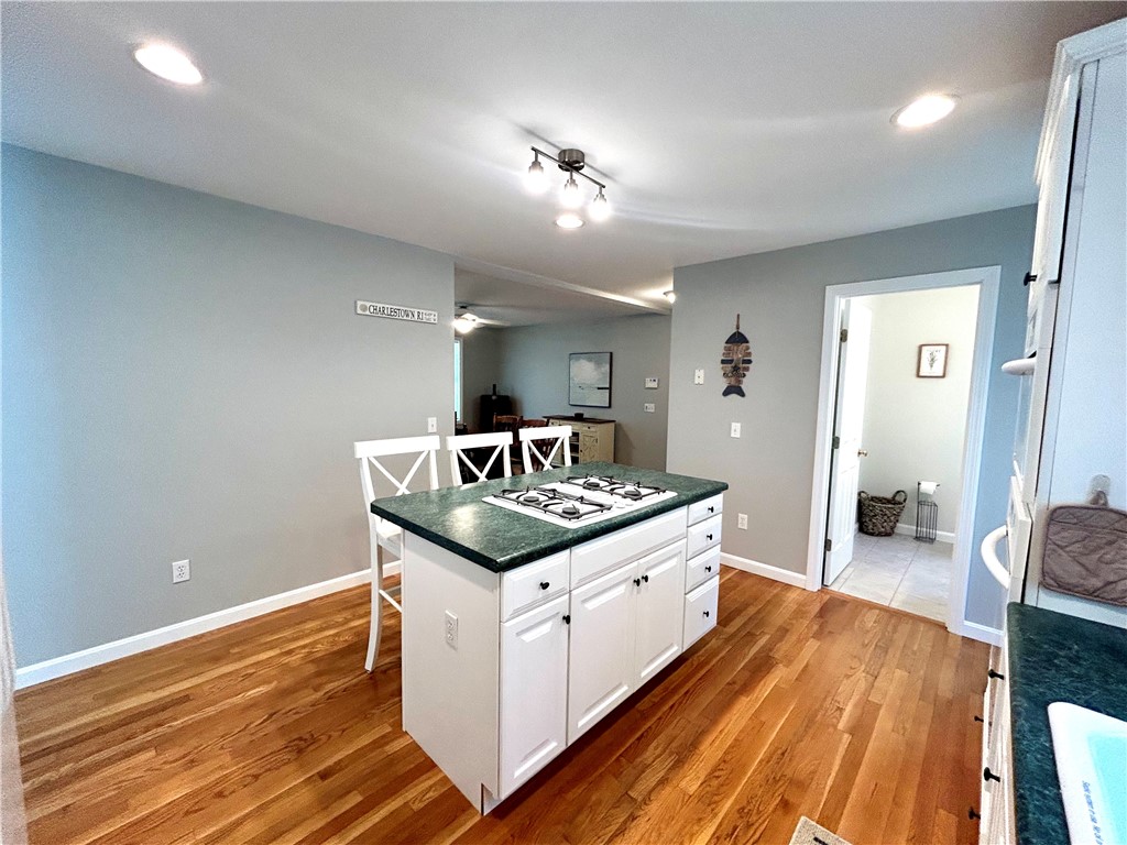 Kitchen with a green stone island, gas cooktop, white cabinetry, and hardwood floors.